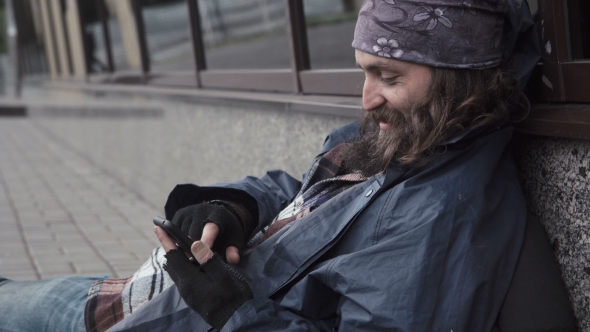 Bearded Begging Man Sitting in Street with Smartphone.