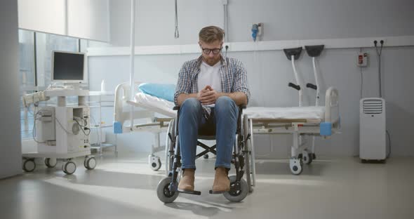 Portrait of Upset Young Man Sitting in Wheelchair in Hospital Ward