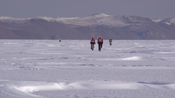 A Group of Cyclists Riding a Bicycle Across a Frozen Lake