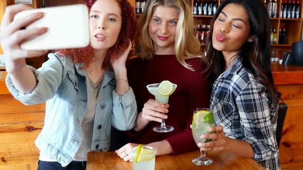 Female friends taking selfie with mobile phone while having drinks 4k