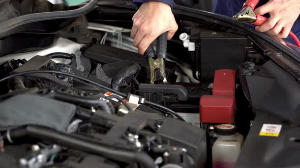 mechanic hand charging battery car with electricity through jumper cables