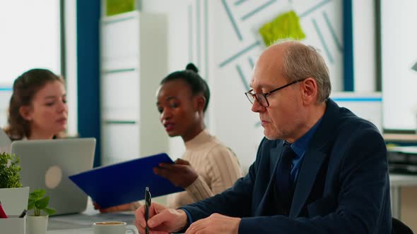 Elderly Businessman Looking at Camera Smiling Sitting in Brainstorming Room