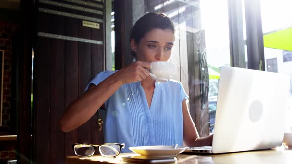 Businesswoman using laptop while having coffee