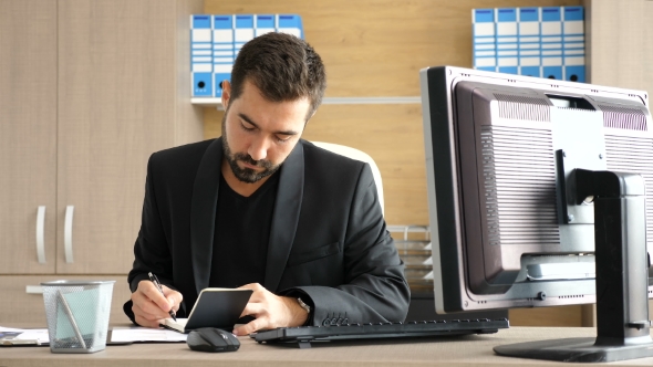 Young Businessman in His Office Taking Notes in a Paper Notebook