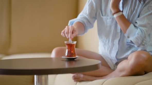 A Woman in a Man's Shirt Stirs Sugar in a Cup, a Lady Drinks Strong Tea and Sits on a Sofa