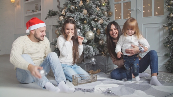 Parent and Two Little Children Having Fun and Playing Together Near Christmas Tree Indoors.