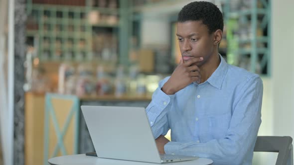 Pensive Young African Man Using Laptop in Cafe 