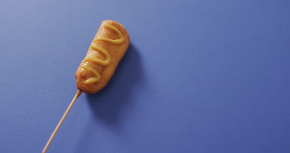 Video of corn dog with mustard on a blue surface