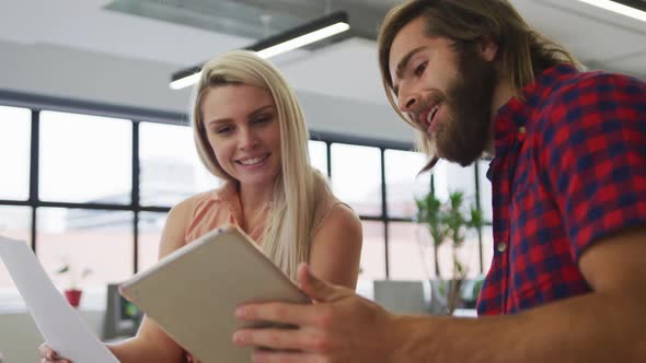 Caucasian business people using digital tablet going through paperwork in modern office