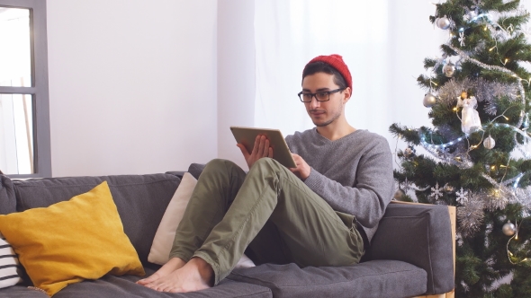 Young Man Using Laptop and Sitting in House near Christmas Tree