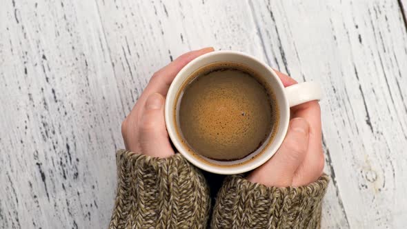 Woman Drinking Coffee and Warms Her Hands. Female Hands in Sweater Holding Cup of Morning Coffee