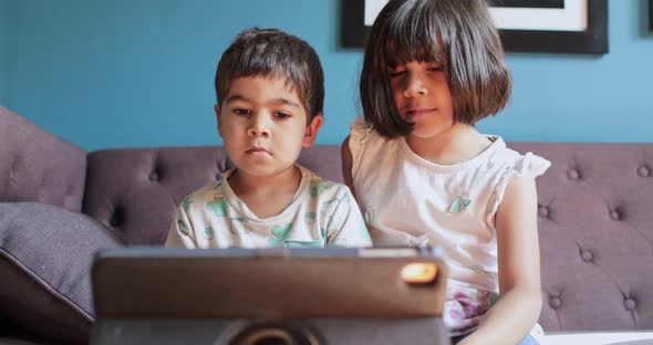 Brother and sister at home during Coronavirus lockdown, sitting on sofa, watching a movie on digital