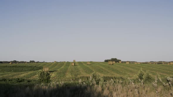 Pan left to right of hay bails in field behind wire fence in Manitoba