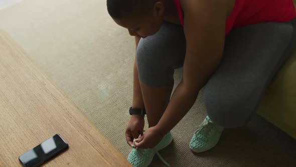 African american plus size woman practicing yoga, tying shoelaces in living room