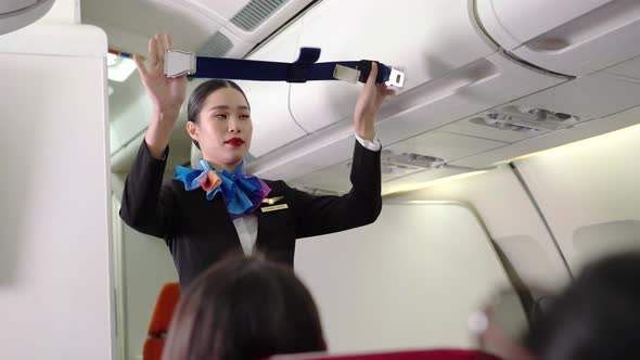 Asian female flight attendant showing safety demonstration on airplane