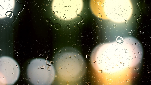Drops of Rain Flow Down the Glass Against the Bokeh Background of Moving Cars alt