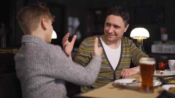 Smiling Father Shaking Hands with Teenage Son Sitting in Restaurant Indoors