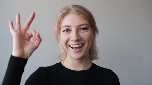 Happy pretty young woman showing ok sign and looking at the camera at home