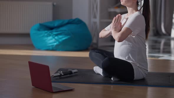 Unrecognizable Pregnant Sportswoman Meditating in Lotus Pose Sitting on Exercise Mat at Home Indoors