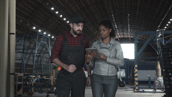 Man Discussing in Aircraft Hangar with Woman