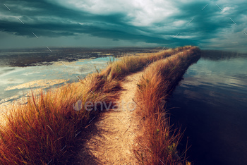 isky footpath road through water vanishing in distance, dark stormy moody clouds bringing bad weather coming towards.