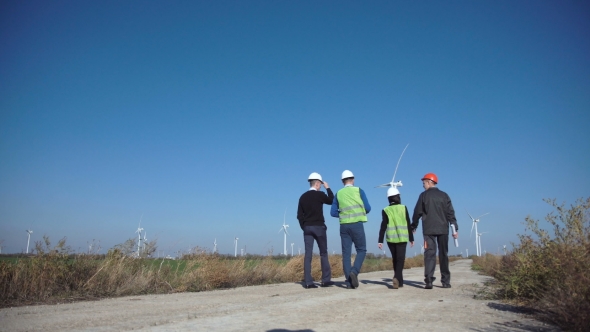 Group of Engineers Walking Against Wind Farm