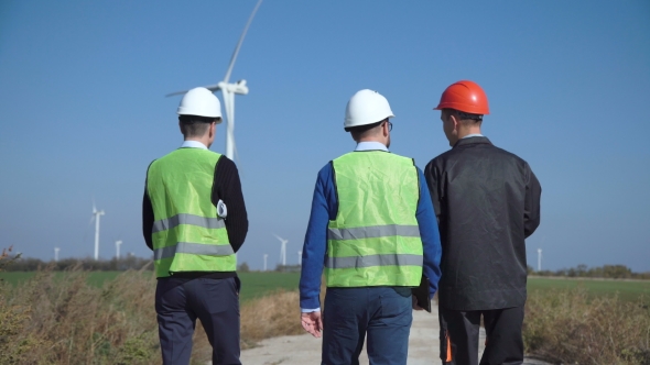 Three Engineers Walking Against Wind Farm