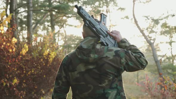 Back View of Soldier Walk to Sunset in Forest with Rifle on Shoulder