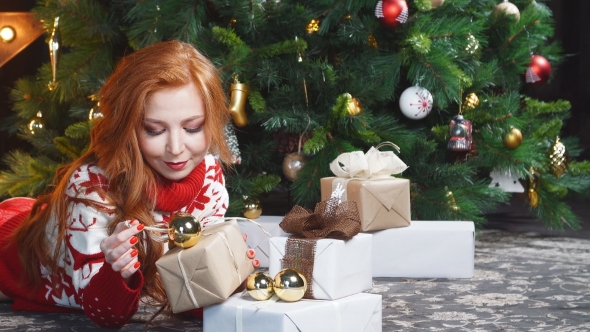Beautiful Redhead Girl in Red Sweater Lying on the Floor with Gift Boxes.