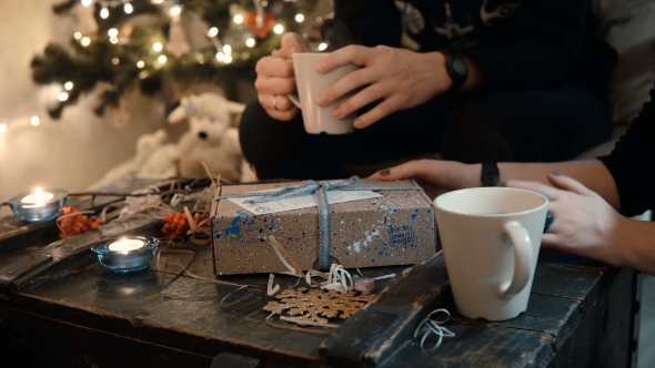 View of Young Couple Sitting at the Table, Near the Christmas Tree and Open the Holidays Present