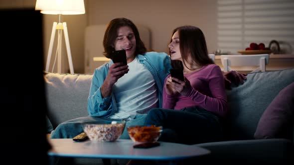 Young Man and Woman Spending Evening Time with Cellphones Woman Peeking Into Man Phone but He Iding