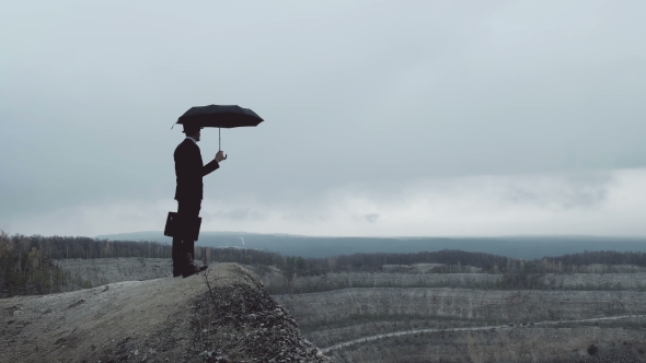 Man with Umbrella on the Top of a Hill and Looks Thoughtfully Into the Distance