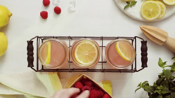 Garnishing raspberry lemonade in drinking mason jars on a white table.