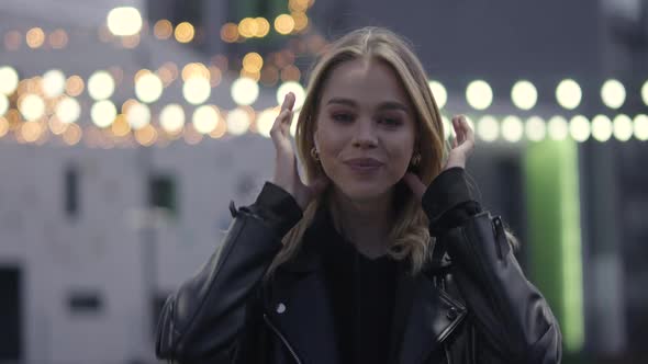 Young Pretty Girl Smiling and Posing on Camera, Near a Modern Residential Area, Evening in the City