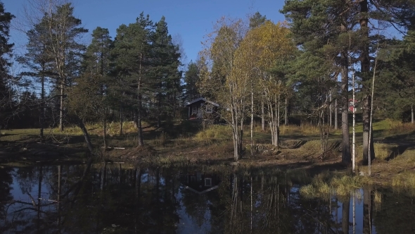 Small Wooden House Near the Edge of a Small River or Pond Amidst Lush Foliage