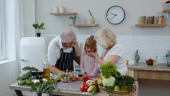 Elderly Grandparents in Kitchen Feeding Grandchild Girl with Chopped Red Pepper. Vegetarian Diet