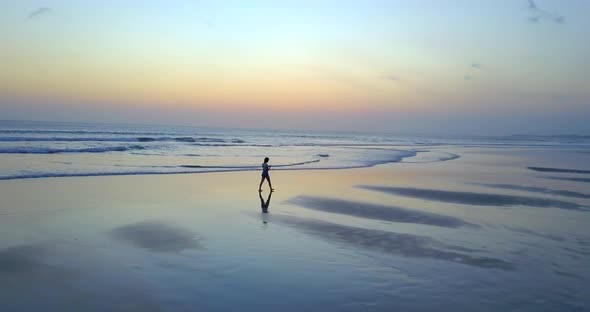 Aerial drone view of a young woman walking on the beach at sunset.