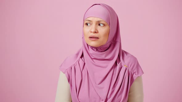 Mature Muslim Woman in Hijab Looking Around and Feeling Frightened Closing Her Mouth in Shock Pink