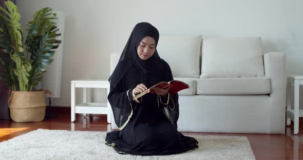 Young Muslim woman wearing traditional clothing and hijab reading Quran