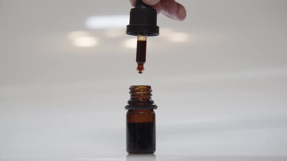 Hand Filling Small Dropper Bottle with CBD Hemp Oil in Laboratory Indoors