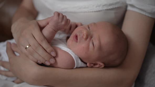 Portrait of Toothless Curios Newborn Boy Lying in Hands of Unrecognizable Mother Looking at Camera