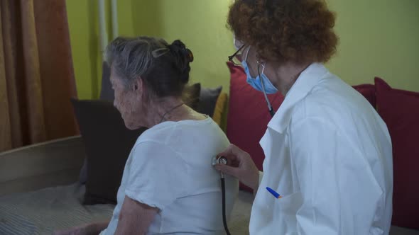 Elderly Female Doctor in White Lab Coat Medical Mask Makes Medical Examination of Senior Woman at