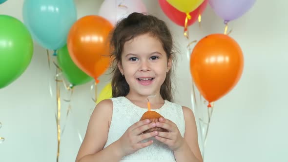 Girl in Dress Smiles Holding Cupcake with Burning Candle
