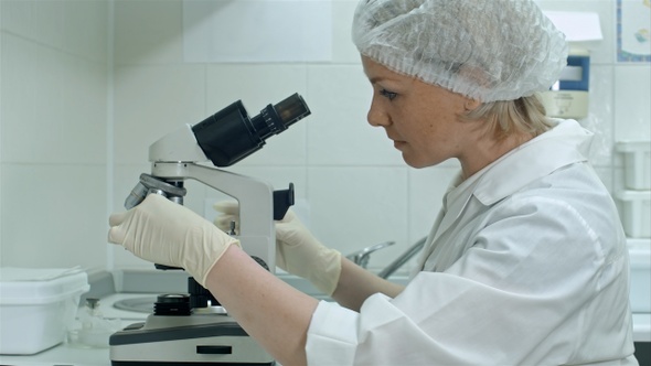 Researcher putting on gloves and using a microscope in a laboratory alt