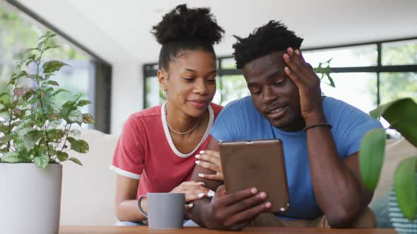 Video of happy african american couple sitting on sofa and using tablet