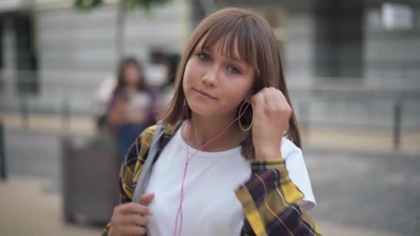 Pretty Confident Teenage Girl Putting Earphones in Ears Dancing Standing on City Street with Blurred