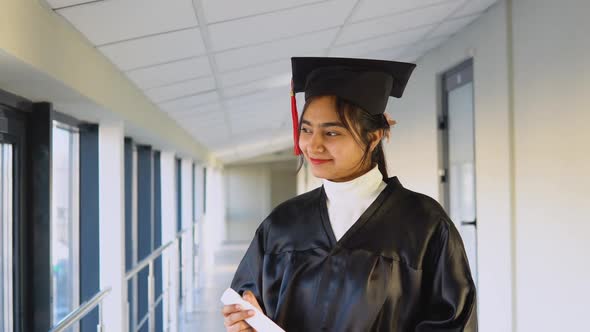 Indian Female Graduate in Mantle Stands with a Diploma in Her Hands and Smiles