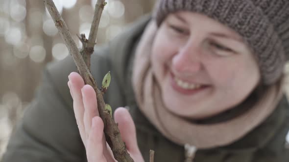 Woman in Warm Clothes Rejoices at Green Buds on Branch on Winter Day