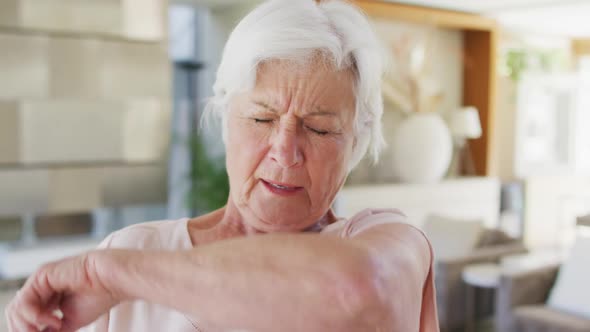 Senior caucasian woman sneezing on her elbow at home