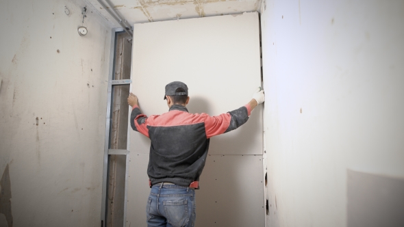 Man Is Lifting Up and Adjusting a Plasterboard on an Aluminum Construction